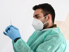 Een man met mondkapje heeft een injectiespuit in zijn hand